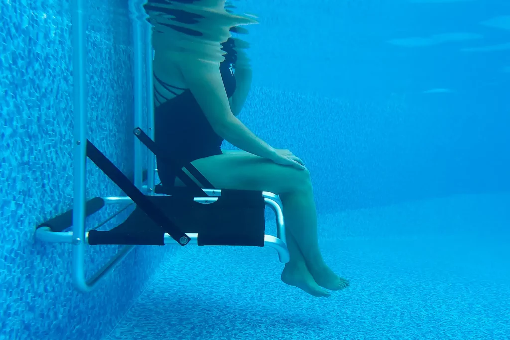 An underwater depiction of a swimmer in a black swim suit sitting partially submerged in the shallow end of a pool using an EdgeMate Pool Chair - a product that can help you supervise your kids as they swim.