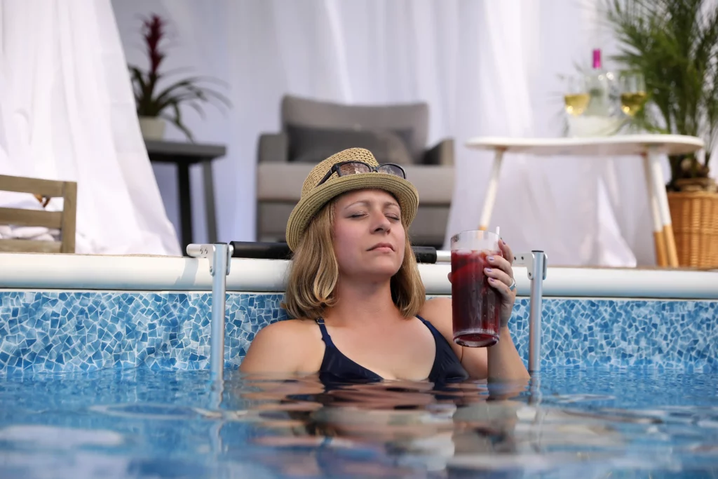 A swimmer sits in an EdgeMate In-Pool Chair and holds a drink while relaxing. By keeping you close to their drink containers, in-pool chairs help you avoid getting dehydrated in a pool.