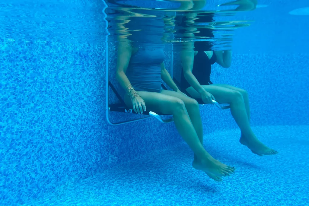 Underwater shot of two swimmers sitting in EdgeMate Pool Chairs situated on the edge of an inground pool. The social interaction and relaxation enhanced by EdgeMate Pool Chairs are an example of how seniors benefit from using a pool.