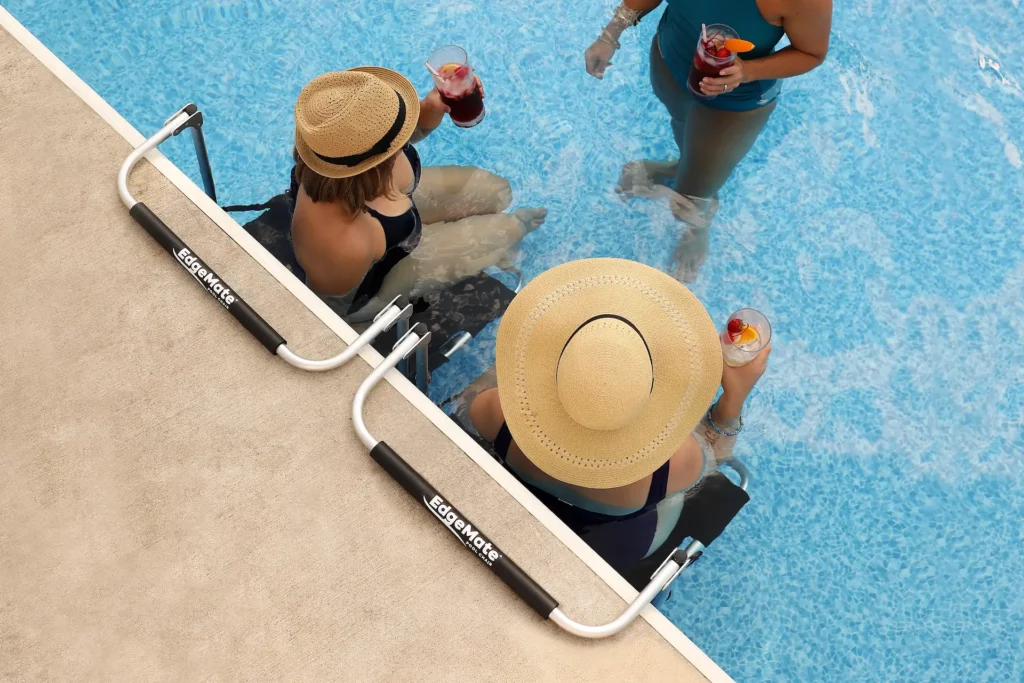 Overhead shot of two swimmers in summer hats enjoying a drink as they sit in EdgeMate in-Pool Chairs and talk to another swimmer standing in the shallow end. These are another option to consider in the in-pool chairs vs. poolside lounge chairs decision.